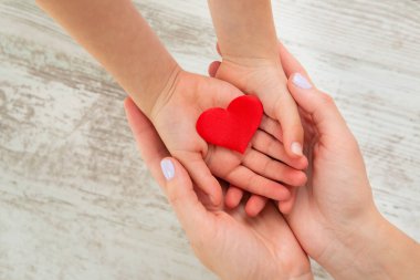 Kırmızı kalp, çocuk ve annenin elleri tahta arka planda. Sağlık ve aile kavramı.