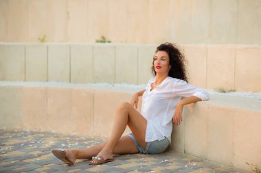 Kıvırcık saçlı, tatilde gülümseyen esmer kadın. Rahat atmosfer.