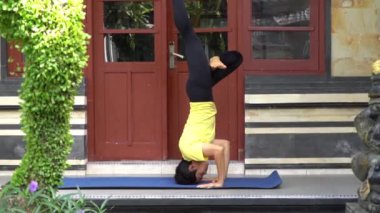 Terasında, çarpıcı görünümlü genç bir Asyalı kız kısa saç kesimi, sarı gömlek ve siyah tayt giyerken yoga çalışıyor. Uzman gibi görünüyor ve mavi Matt üzerinde Yoga yapıyor.