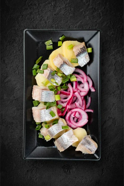 Hafif tuzlanmış ringa balığı, haşlanmış patates ve soğanlı aperatif. Siyah bir arka planda izole edilmiş. Üst görünüm