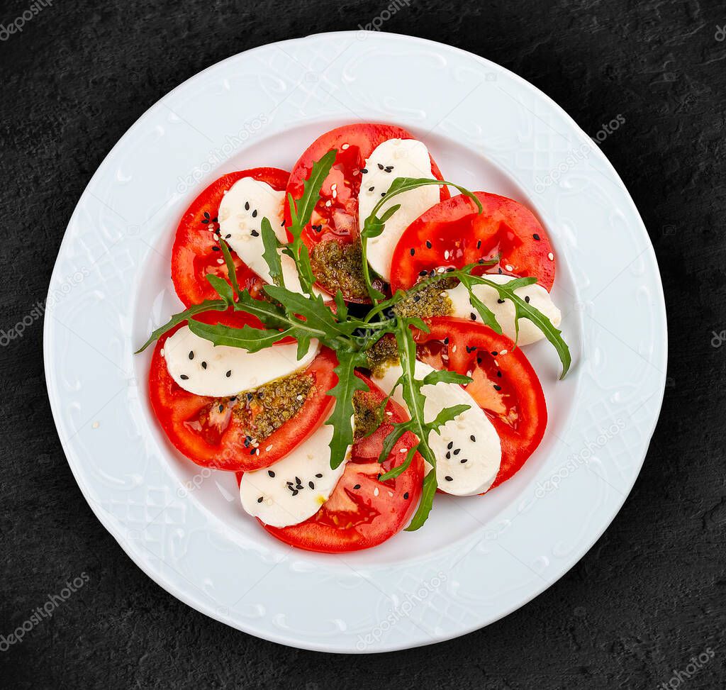 Caprese salad with mozzarella, tomatoes and pesto sauce. A traditional Italian dish. Isolated on a black background.