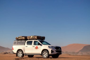 Güneşli bir günde Namib Çölü 'nün kırmızı kumlarında beyaz bir araba duruyor. Sossusvlei, Namibya