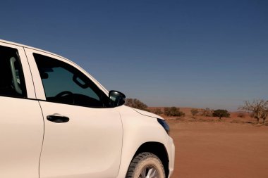 Güneşli bir günde Namib Çölü 'nün kırmızı kumlarında beyaz bir araba duruyor. Sossusvlei, Namibya