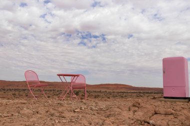 İki pembe sandalye, bir masa ve Namib Çölü 'nde bulutlu bir gökyüzünün arka planında duran bir buzdolabı. Namibya