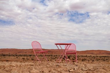 Namib Çölü 'nde bulutlu bir gökyüzünün zeminine karşı iki pembe sandalye ve bir masa standı. Namibya