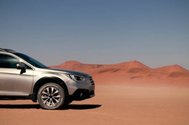 Güneşli bir günde Namib Çölü 'nün altın kumlarında gri bir araba duruyor.. 