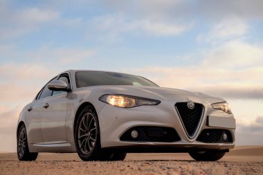 Alfa Romeo Giulia bulutlu gökyüzüne karşı altın kumda duruyor. 01.07.2021. Svakopmund. Namibya. Afrika