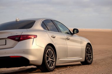 Alfa Romeo Giulia bulutlu gökyüzüne karşı altın kumda duruyor. 01.07.2021. Svakopmund. Namibya. Afrika