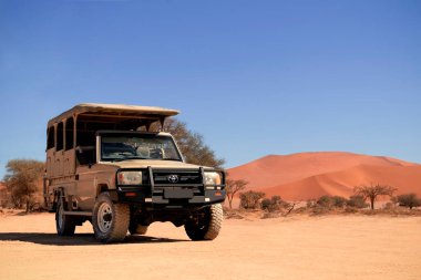 Güneşli bir günde Namib Çölü 'nün kırmızı kumlarında bir off-road arabası duruyor. Sossusvlei, Namibya. Afrika