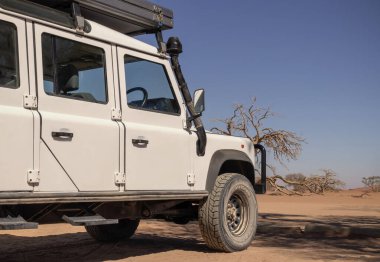 Güneşli bir günde Namib Çölü 'nün kırmızı kumlarında beyaz bir off-road arabası duruyor. Sossusvlei, Namibya