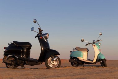 Namib Çölü 'nün altın kumlarında gün batımında iki tane Retro scooter.