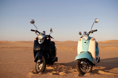 Namib Çölü 'nün altın kumlarında gün batımında iki tane Retro scooter.
