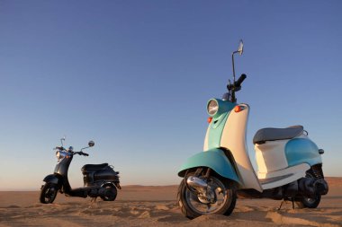 Namib Çölü 'nün altın kumlarında gün batımında iki tane Retro scooter.