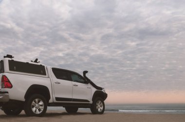 Beyaz off-road arabası Atlantik okyanusunun kıyısında duruyor. Parlak dramatik bir günbatımında.