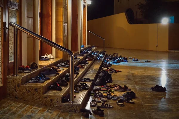 Muslims people take off shoes on the steps in front of mosque entrance before friday evening prayers worship. Footwear outside a mosque during prayer time on dark blurred background.Soft focus. — Stock Photo, Image