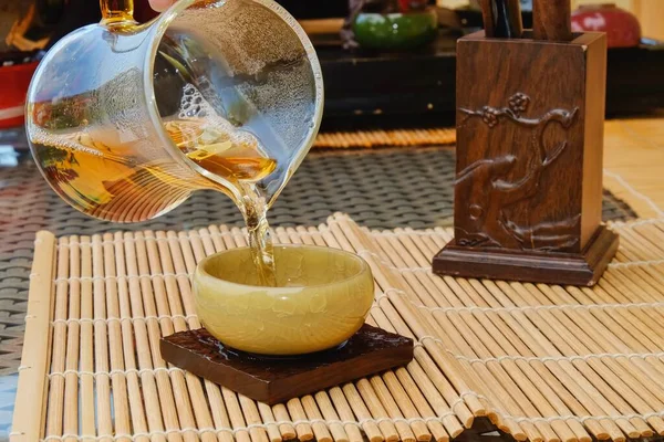 Fragmento de té tradicional sirven en la ceremonia del té. Misted transparente con gotas de condensado tetera de vidrio con té verde y especial semi-brillo verde claro esmaltado tazón de té de cerámica crepitante en primer plano —  Fotos de Stock