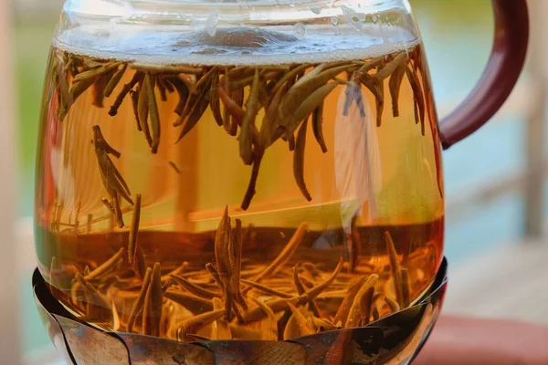 Floating brewing green tea leaves in blurred motion close up inside a transparent glass kettle on natural blurred background during tea ceremony in Japanese Zen garden — Stock Photo, Image