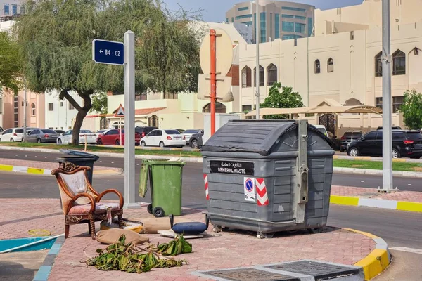 Obsolete arabic style home furniture thrown near garbage container on city street.Old oriental armchair near plastic trash dumpster can. Getting rid of old junk. Recycling industry.Urban ecology. — Stock Photo, Image