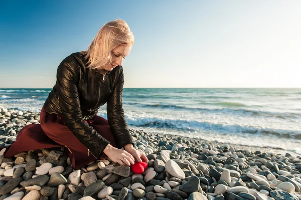 Blond Girl on the seaside hiding a heart — Stock Photo, Image