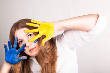 Genç kadın elleriyle yüzünü örterek kendini savunuyor. Ellerini Ukrayna bayrağı rengine boyamış. Beyaz arka planda izole edilmiş..