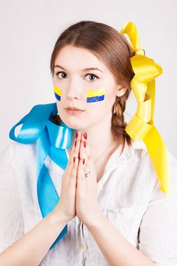 Yanaklarında Ukrayna bayrağı olan korkmuş genç bir kadın beyaz arka planda izole edilmiş Ukrayna halkının ve barış için dua ediyor..