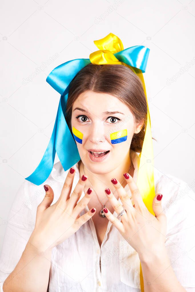 Scared young pretty woman with a painted Ukrainian flag on her cheek isolated on a white background.