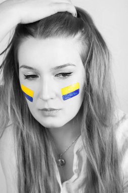 Yanaklarında Ukrayna bayrağı olan üzgün genç bir kadın beyaz arka planda izole edilmiş. Siyah beyaz fotoğraf..