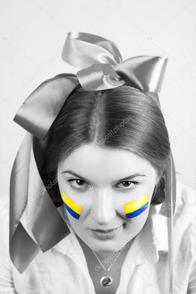 Portrait of a young woman with a painted Ukrainian flag on her cheeks with a sly smirk isolated on a white background. Black and white photography.