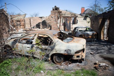 Bucha, Kyiv bölgesi - 5 Mayıs 2022: Şehrin bombalanmasından sonra yanan araba yıkılmış bir evin avlusunda duruyor. Rusya ile Ukrayna arasındaki savaş, 5 Mayıs 2022.