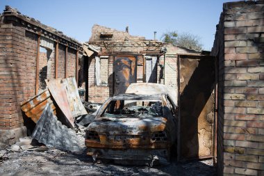 Bucha, Kyiv bölgesi - 5 Mayıs 2022: Şehrin bombalanmasından sonra yanan araba yıkılmış bir evin avlusunda duruyor. Rusya ile Ukrayna arasındaki savaş, 5 Mayıs 2022.