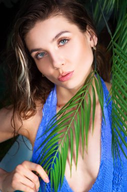 Portrait of a young woman in water drops near a palm tree on a black background.
