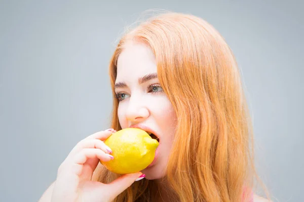 Young beautiful woman eating lemon isolated on gray background. Healthy eating concept. Diet.