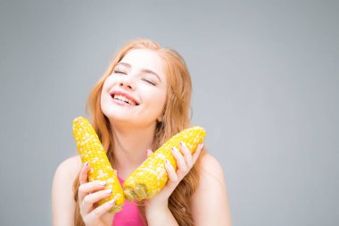 Happy young woman holding corn isolated on gray background. Healthy eating concept. Diet.