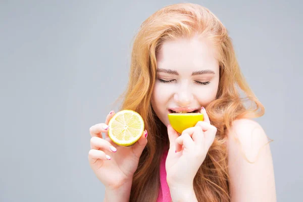 Funny young woman eating lemon isolated on gray background. Healthy eating concept. Diet.