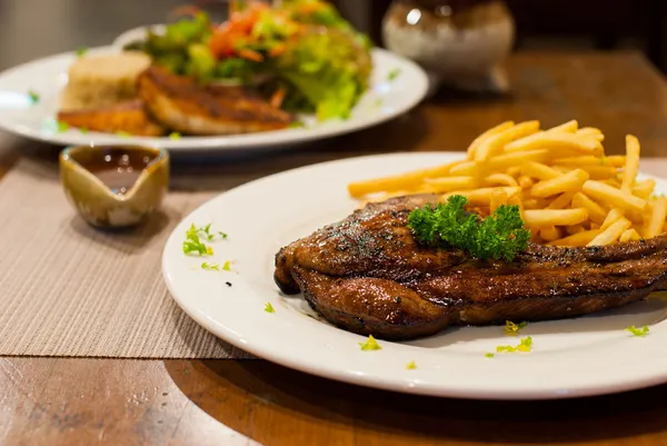 Pork chop gegrilde biefstuk met Franse frietjes, de top met peterselie. — Stockfoto