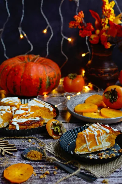 Vertikale herbstliche Komposition in Orangetönen. Kürbiskuchen mit Quark und saftigen Kaki auf rustikalem Hintergrund — Stockfoto