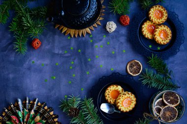 Karanlık bir arkaplanda yılbaşı planı. Reçelli bisküvi, çaydanlık, ladin dalları, dekor. Üst görünüm, alanı kopyala.