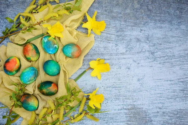 Composizione con uova di Pasqua colorate su un tovagliolo giallo con boccioli primaverili e fiori gialli su sfondo blu. Layout, spazio di copia — Foto Stock