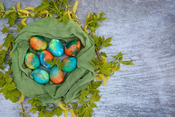 Uova di Pasqua dipinte in un nido decorativo di rami verdi e tovaglioli su uno sfondo blu. Vista dall'alto. Copia spazio — Foto Stock
