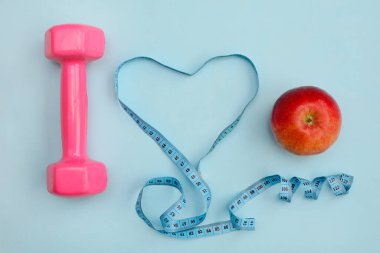 Bir elma, kalp şeklinde bir mezura ve mavi arka planda bir dambıl. Fitness konsepti
