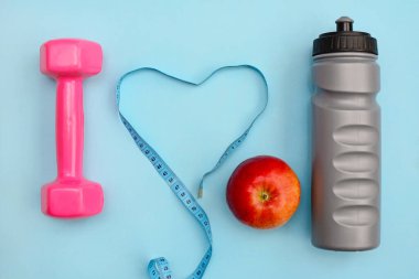 Fitness konsepti ve sağlıklı yaşam tarzı. Dambıllar, şişe, elma ve kurdele mavi arka planda, üst manzara