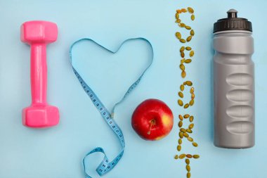 Mavi arka planda bir düzen. Spor ve spor aletleri. Dambıllar, şişe, elma, kurdele ve yazıt Spor