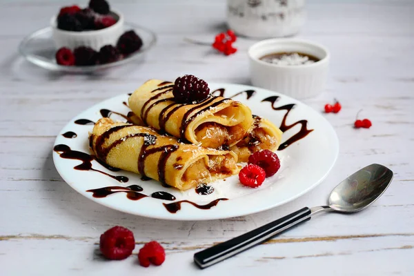 Pannenkoeken met chocolade en bessen op een wit bord op een lichte houten achtergrond. Ontbijt — Stockfoto