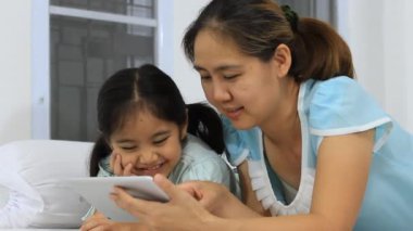 Küçük Asya anne ve kızı kullanarak yatağa tablet