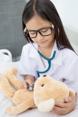 Asyalı kız doktor stetoskop ve ayı oyuncak bebekle oynarken