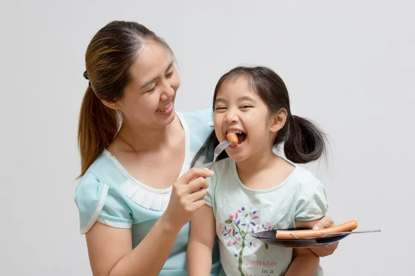 Asian mother feeding sausage to her daughter — Stock Photo, Image