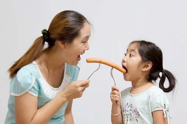 Asian mother feeding sausage to her daughter — Stock Photo, Image