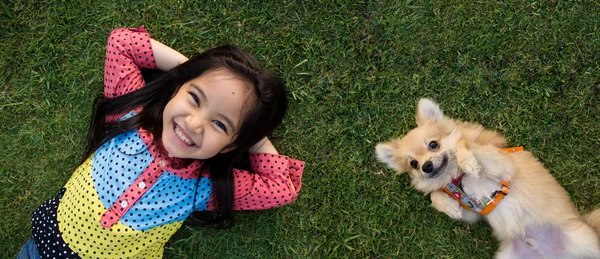 Gelukkig Aziatisch meisje met haar hondje portret liggend op gazon — Stockfoto