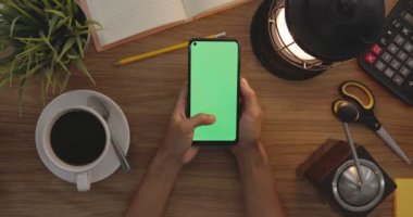 Top View Woman Uses Thumb Touching On Green Screen Of Smart Phone. Hobby Table Background. Chroma Key. Mobile Phone With Green Screen.