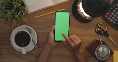 Top View Woman Uses Finger Touch On Green Screen Of Smart Phone. Hobby Table Background. Chroma Key. Mobile Phone With Green Screen.